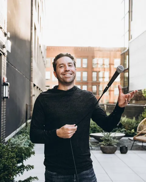 Rob Cressy smiling and holding out a microphone on a rooftop patio